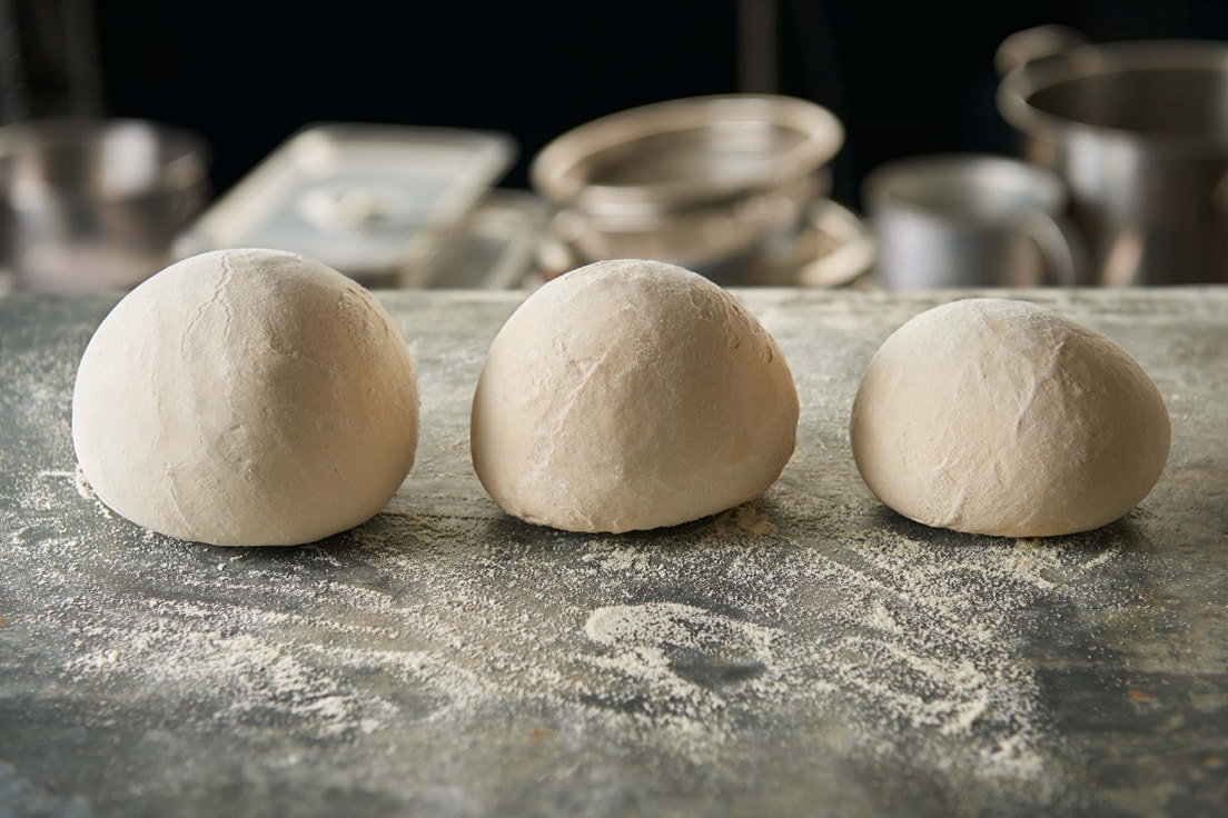 three pizza dough balls resting on a slab